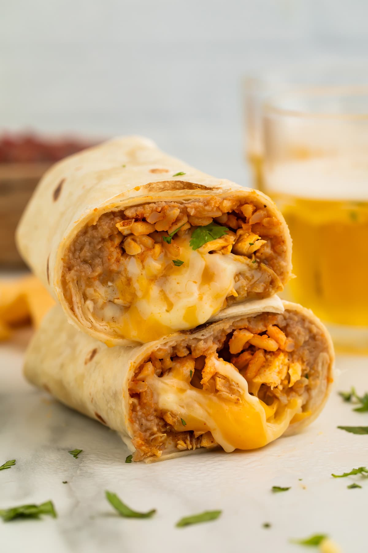 Two halves of a chicken burrito stacked on top of each other, showing a filling of chicken, rice, beans, and gooey cheese.