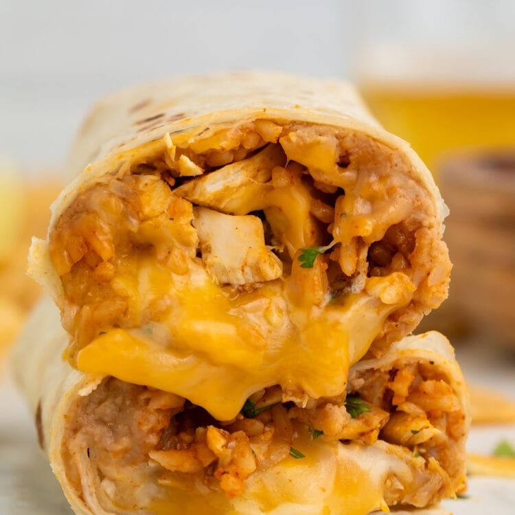 Two halves of a chicken burrito stacked on top of each other, showing a filling of chicken, rice, beans, and gooey cheese.