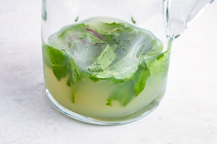 Simple syrup and white rum in a pitcher with muddled mint leaves and fresh lime juice.
