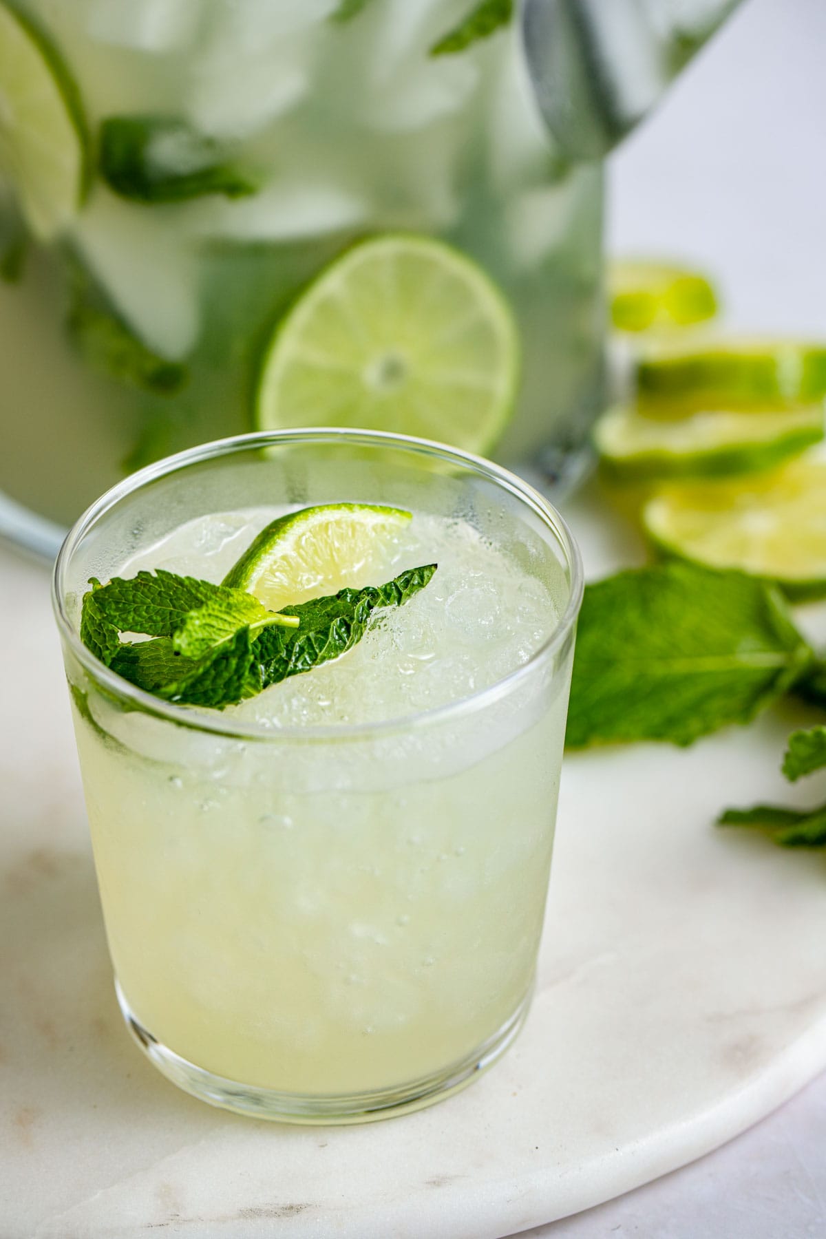 Close up of a glass of mojito in front of a pitcher of mojitos