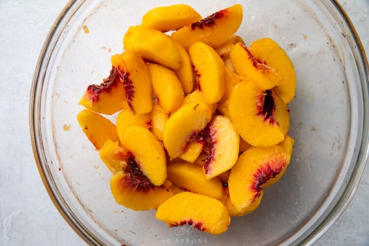 Peach slices in a glass mixing bowl with lemon juice