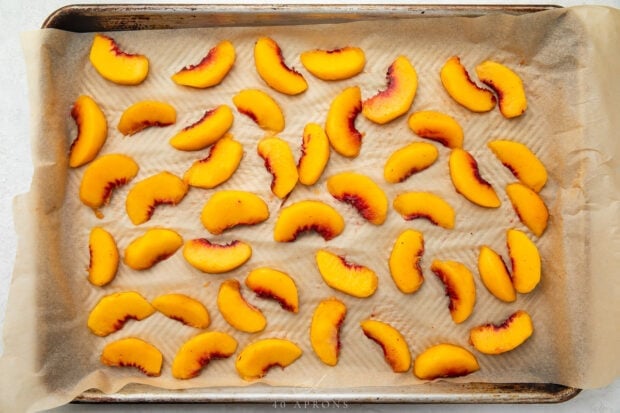 Unfrozen peach slices on a baking sheet lined with parchment paper