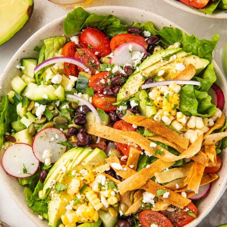 Overhead angle of Mexican salad with tortilla strips in a white bowl, next to a glass of chelada and limes.