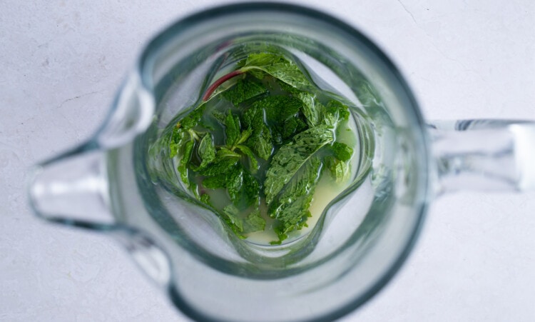 Mint leaves and lime juice in the bottom of a glass pitcher