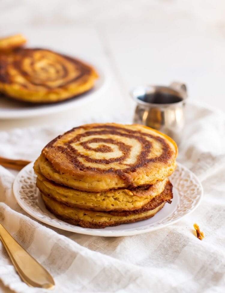 A stack of paleo cinnamon roll pancakes on a white plate on a white tablecloth