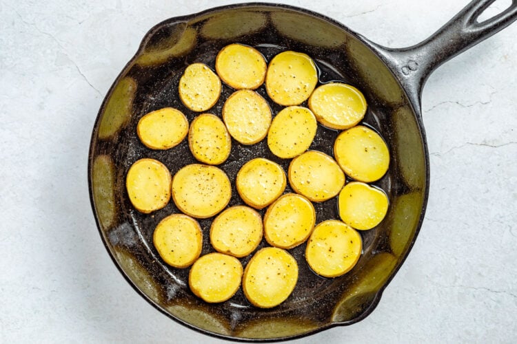 Partially fried potato slices in a large cast-iron skillet.