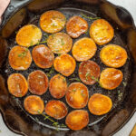 Top-down view of pan fried potatoes in a single layer in a large black cast iron skillet on a marble countertop.
