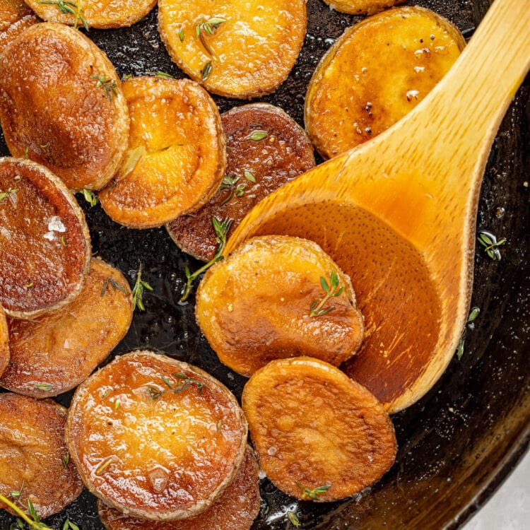 Crispy, pan fried potatoes in a black cast-iron skillet with a wooden spoon.