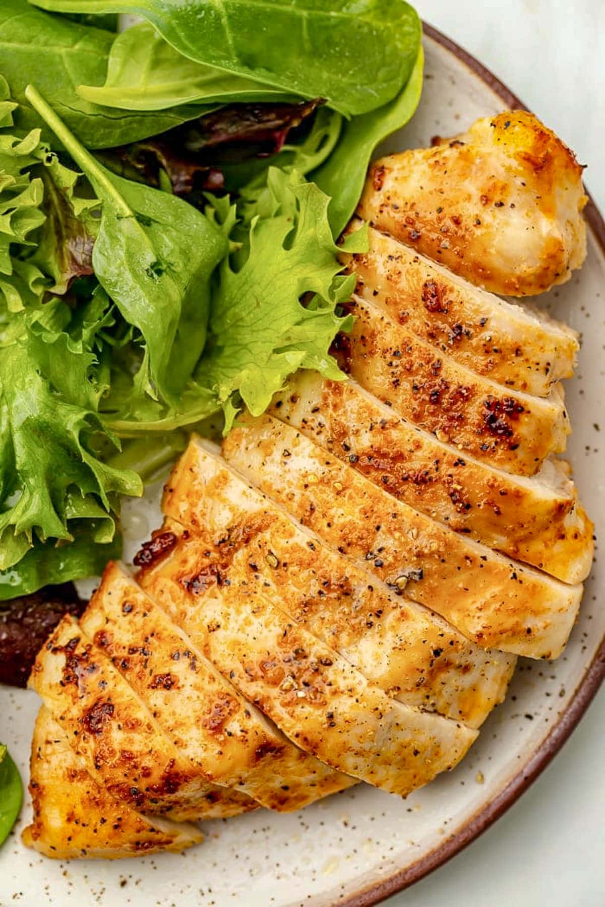 A chicken breast, cooked in the air fryer, sliced and plated with a small green leaf salad.