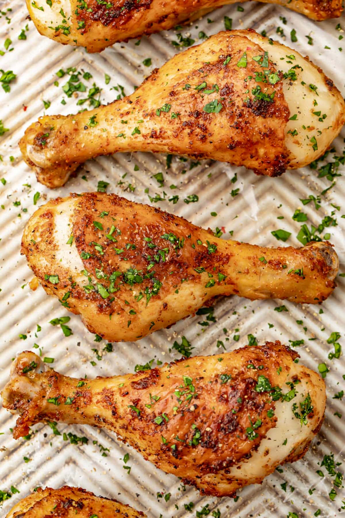 Top-down photo of seasoned air fryer chicken legs on a baking sheet with fresh herbs.
