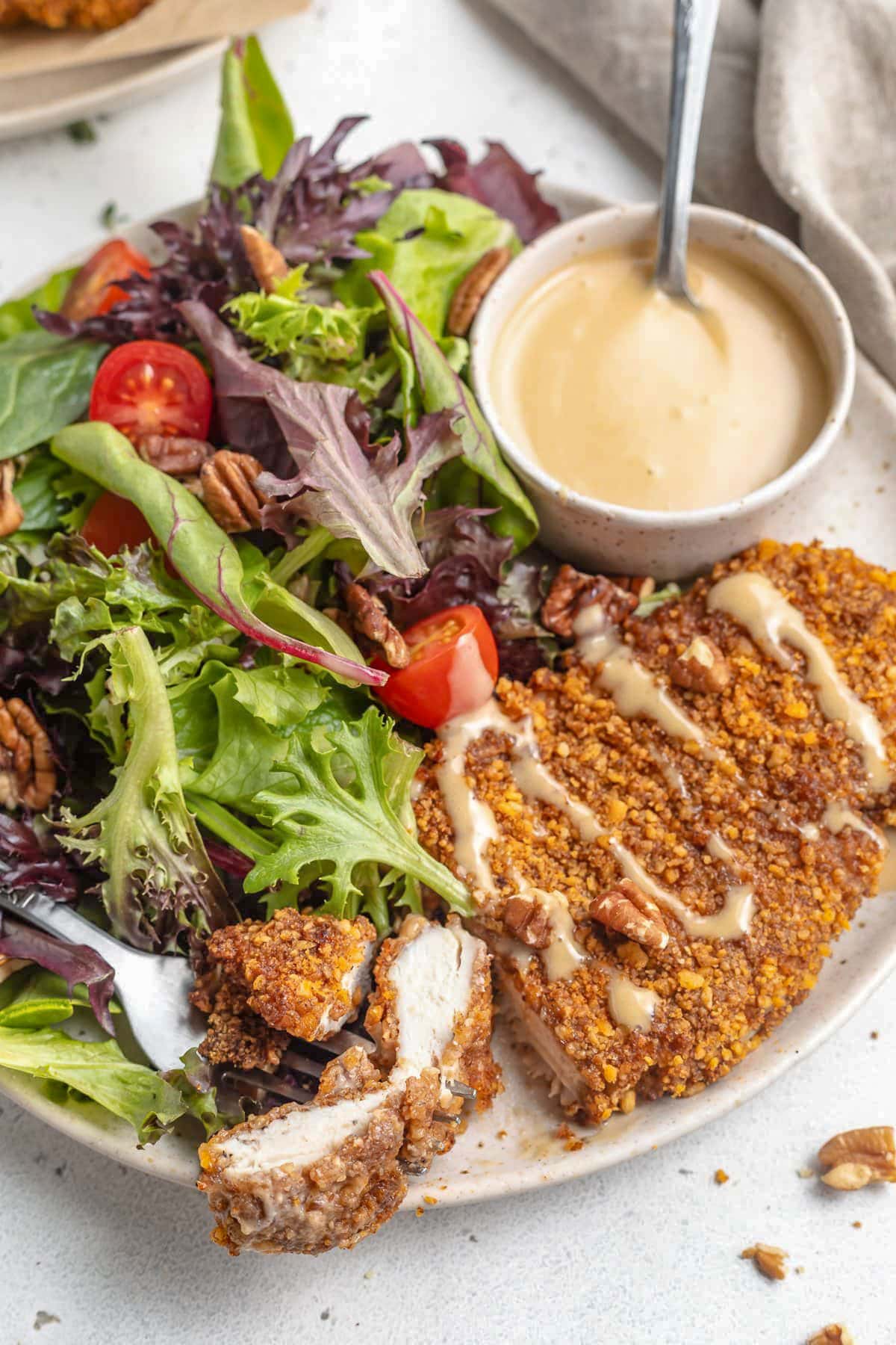 A crispy, pecan-crusted chicken breast cooked in the air fryer then plated with a small salad and a ramekin of honey mustard.