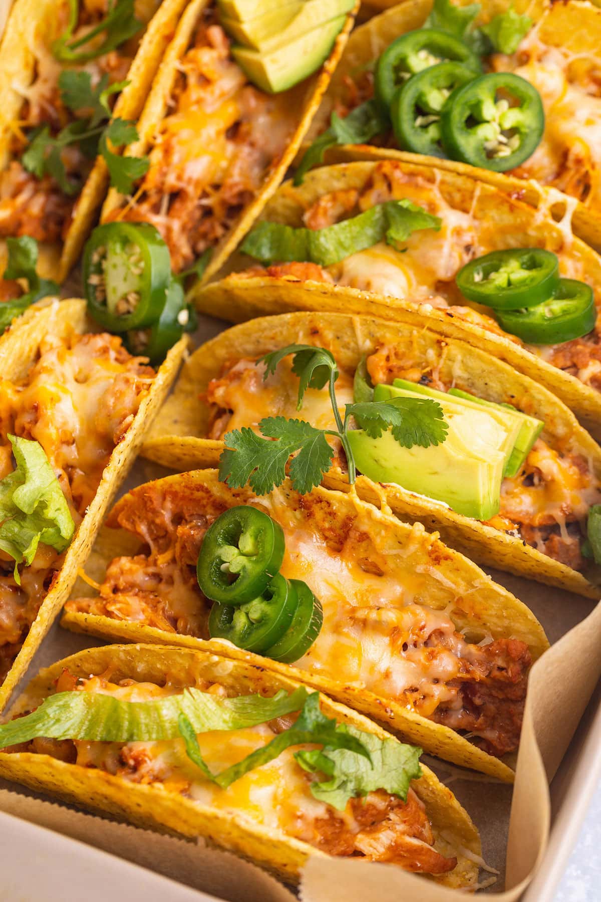 Baked chicken tacos in crunchy taco shells, lined up in a baking pan.