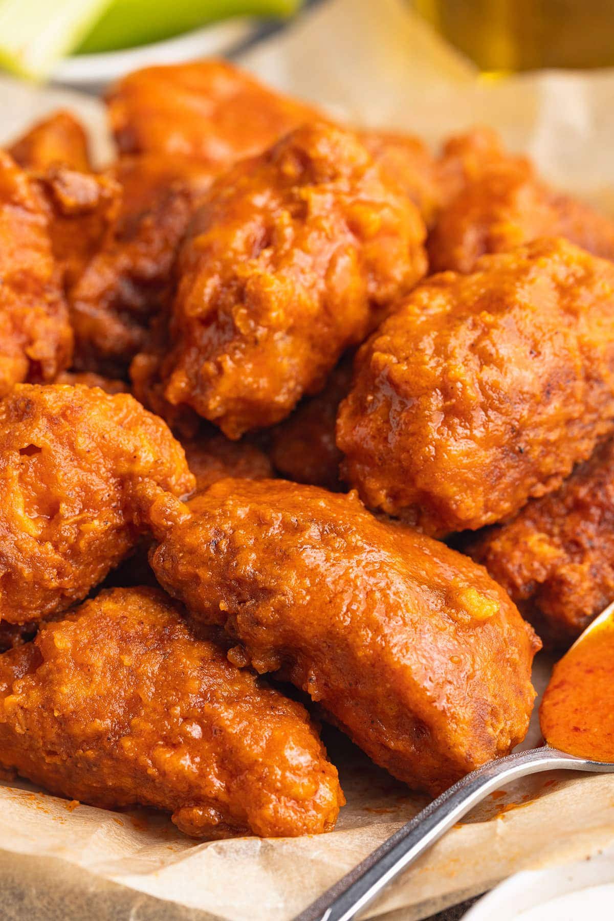 A pile of boneless buffalo chicken wings in a shallow bowl lined with parchment paper.