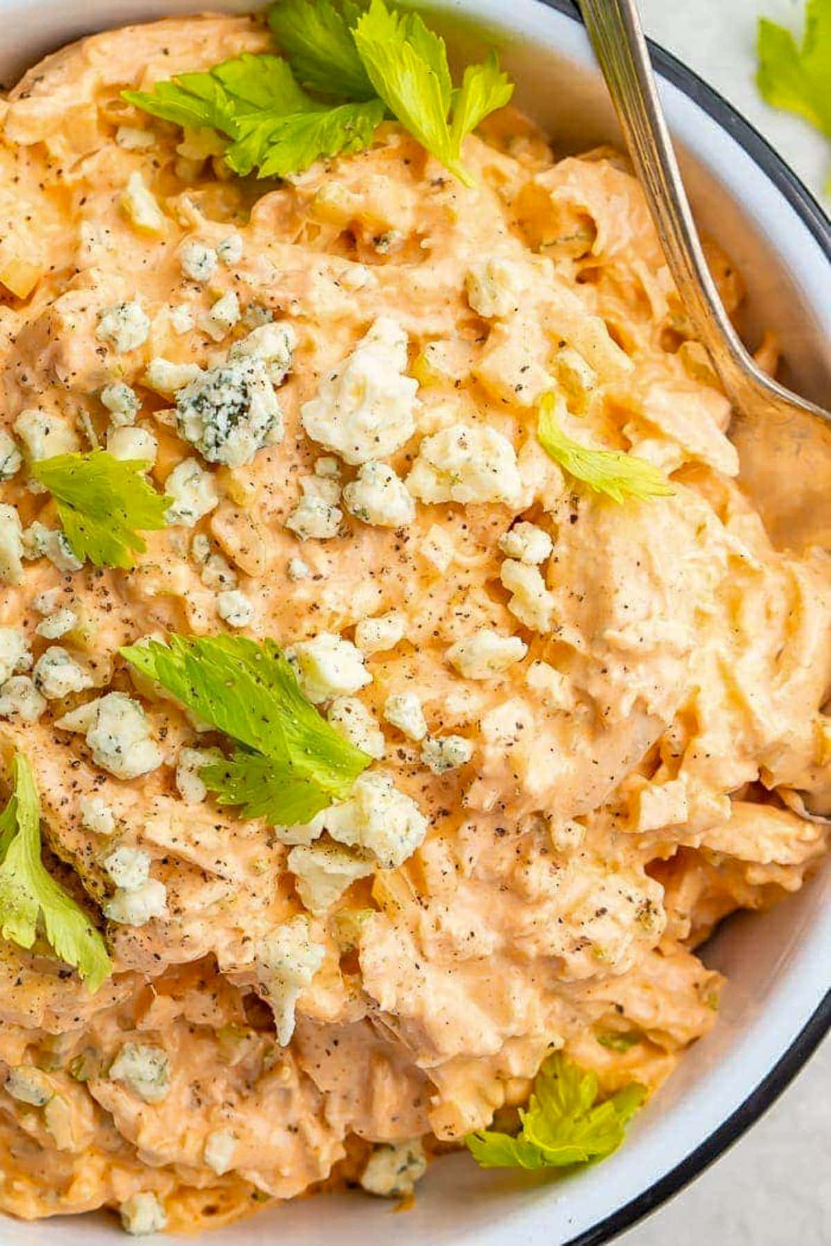 A large bowl filled with creamy buffalo chicken salad topped with blue cheese crumbles and fresh herbs.