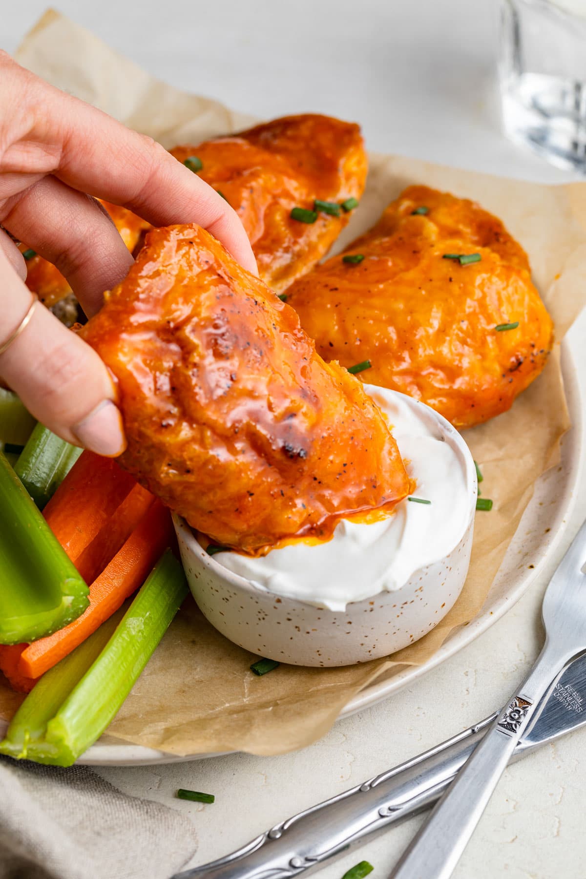A buffalo sauced chicken thigh being dipped into a bowl of blue cheese dressing.