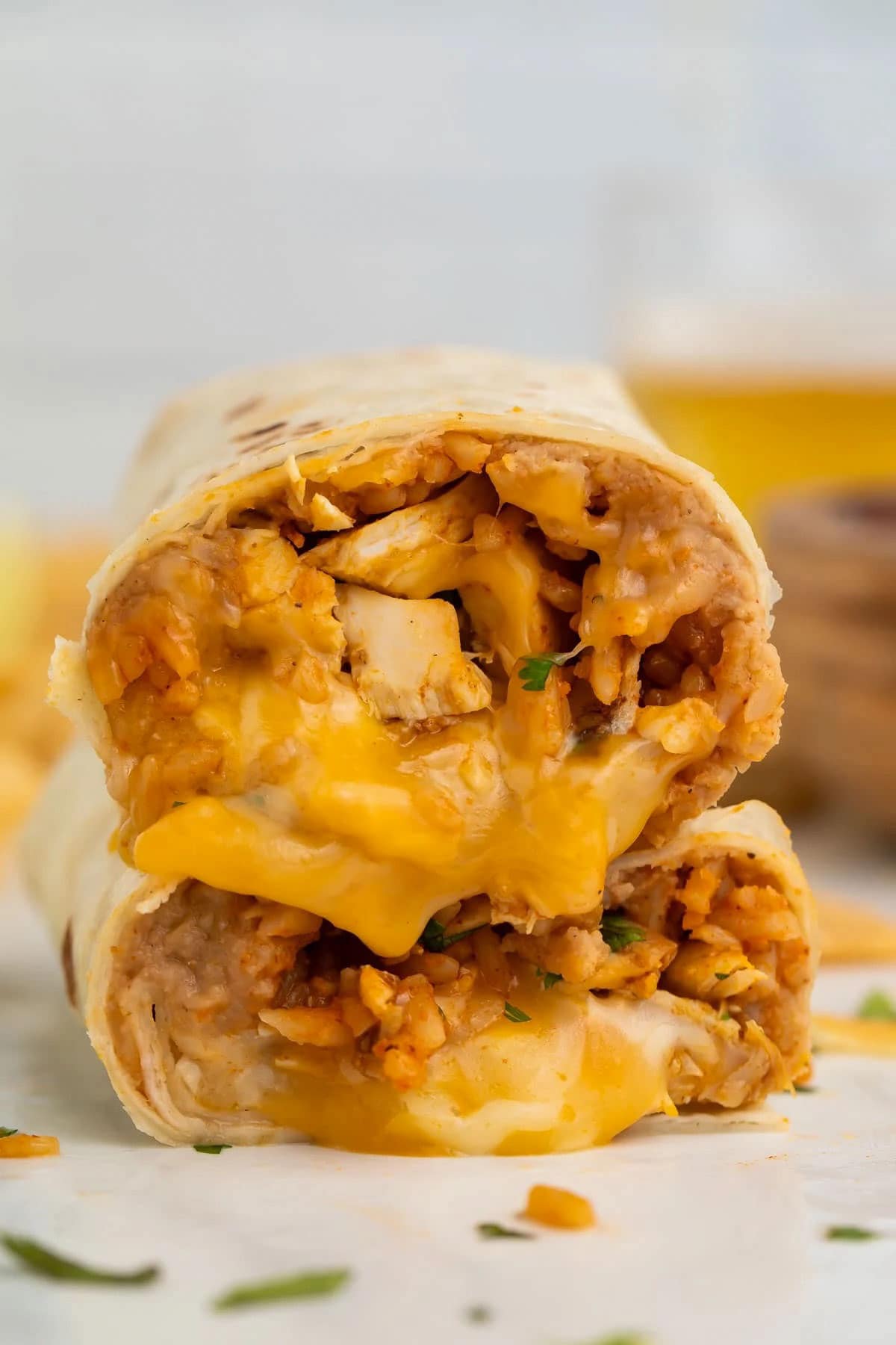 Two halves of a bean and chicken burrito with melted cheese, stacked on top of each other to show the filling inside.
