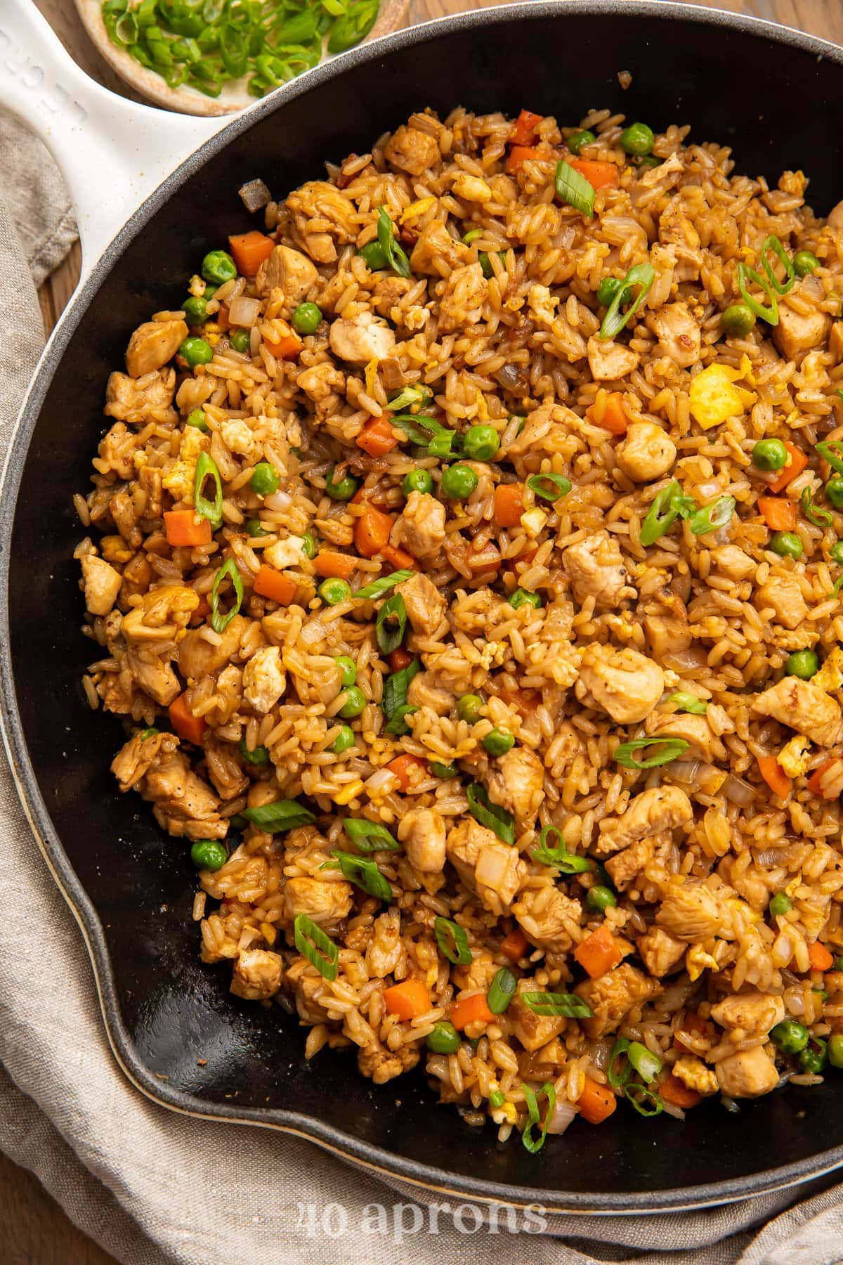 Overhead photo of chicken fried rice with mixed veggies in a large black cast iron skillet.
