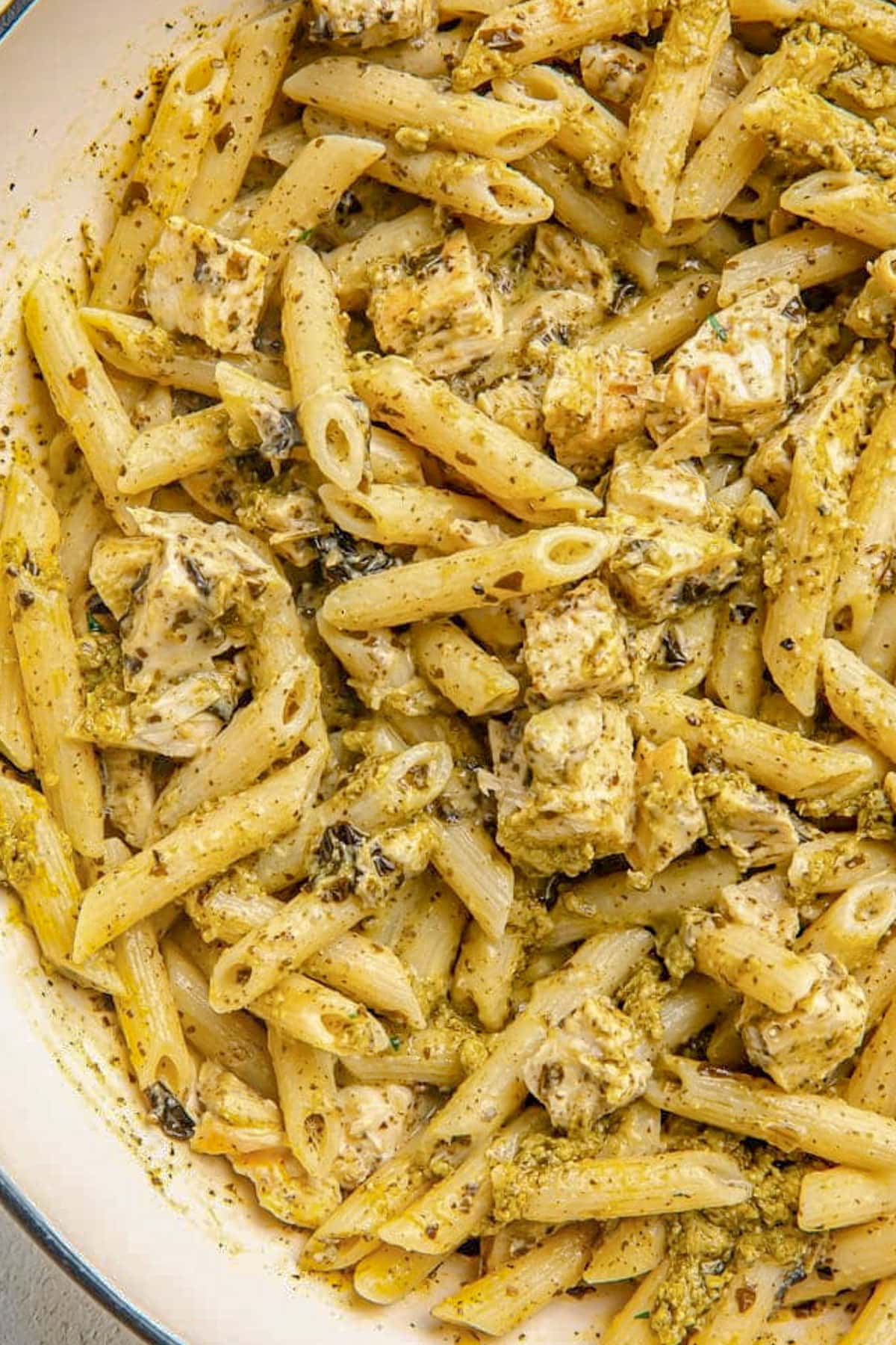 Close up of pesto penne pasta with grilled chicken in a large pot.