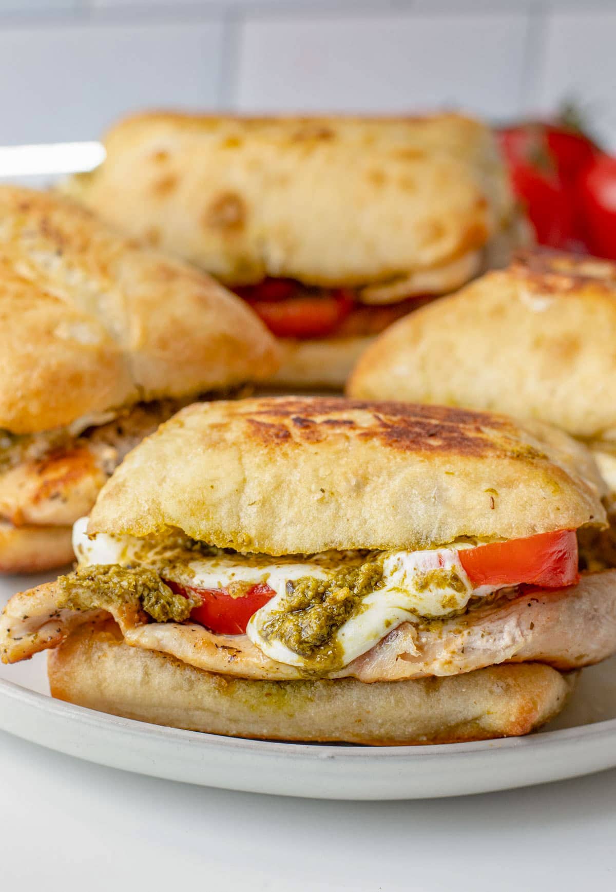 4 chicken pesto sandwiches with tomato and cheese on a plate.
