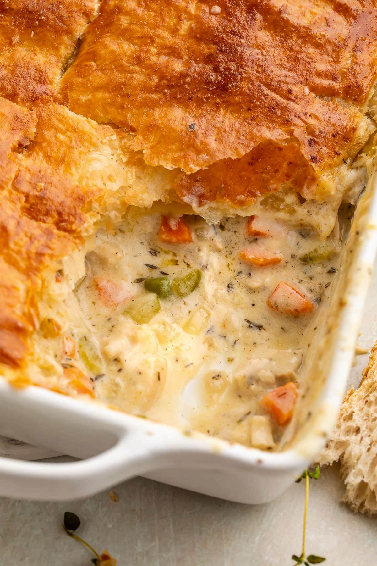 Close-up of a corner of a square casserole dish holding a chicken pot pie casserole, with one scoop of casserole missing.
