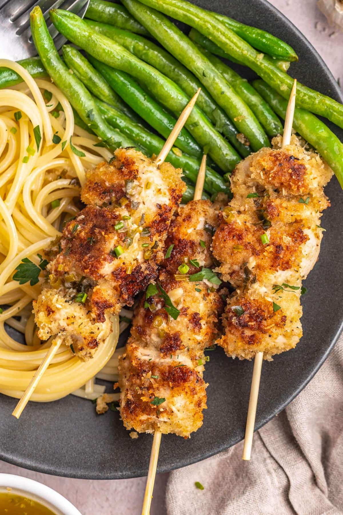 Skewered chicken spiedini on a grey plate with bright green asparagus and thin pasta.