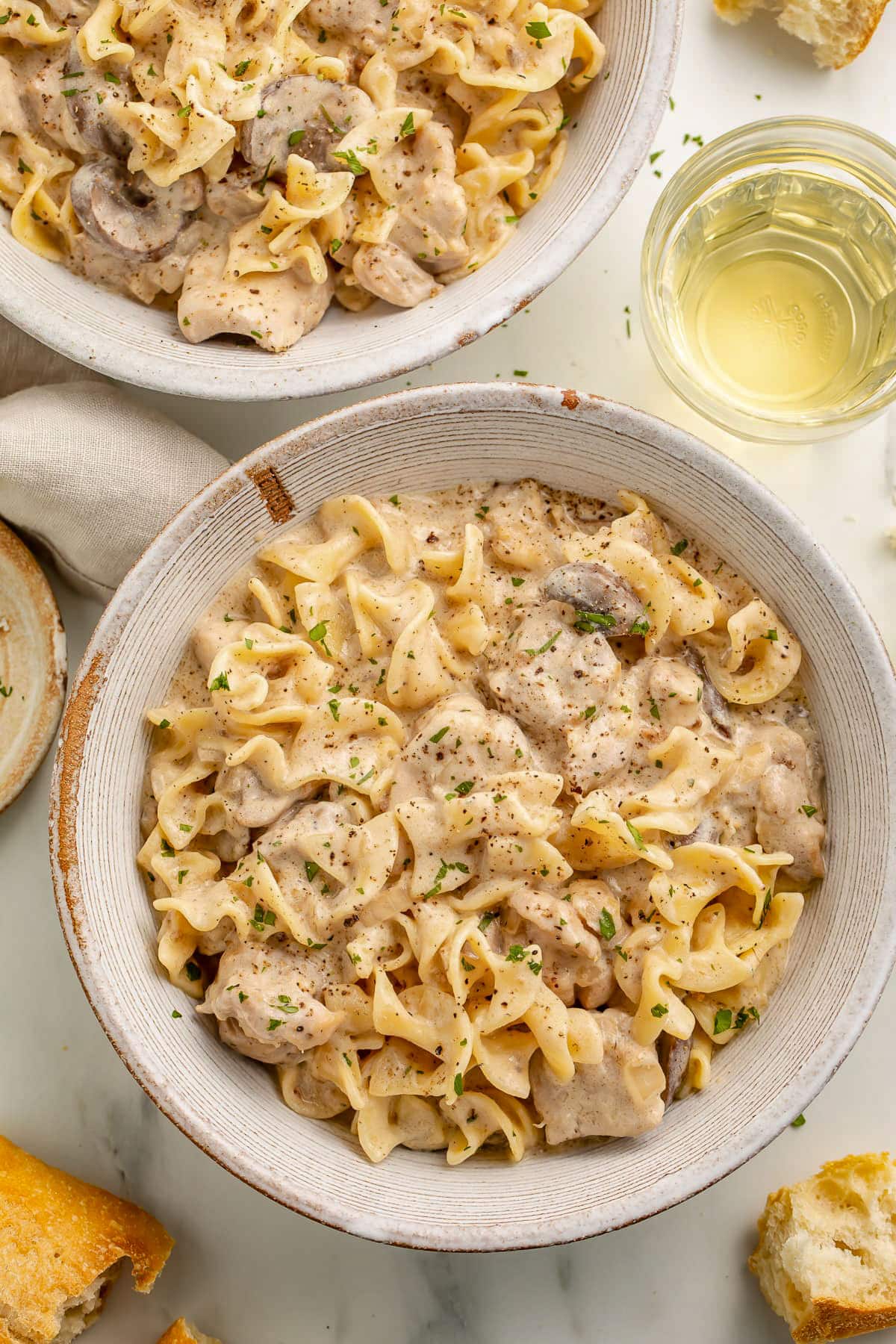 Two bowls of chicken stroganoff with tender, thick noodles and a creamy gravy.