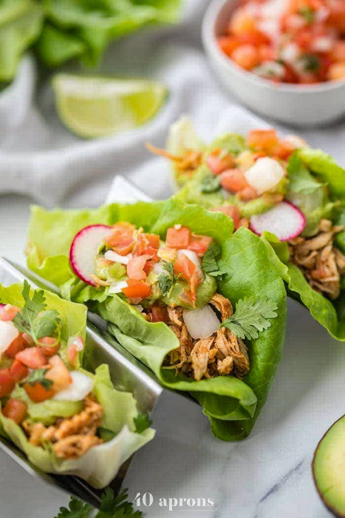 3 chicken tacos in lettuce wraps topped with sliced radishes and pico de gallo in a taco holder.