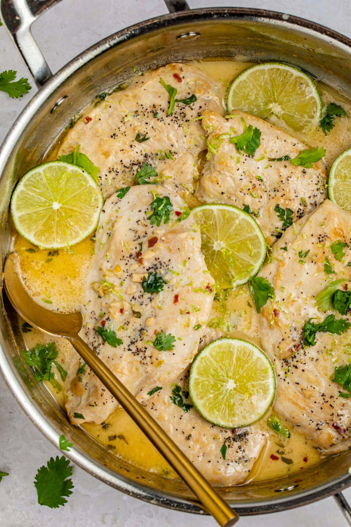 A large skillet containing seared chicken breasts with a creamy coconut lime sauce and discs of limes.