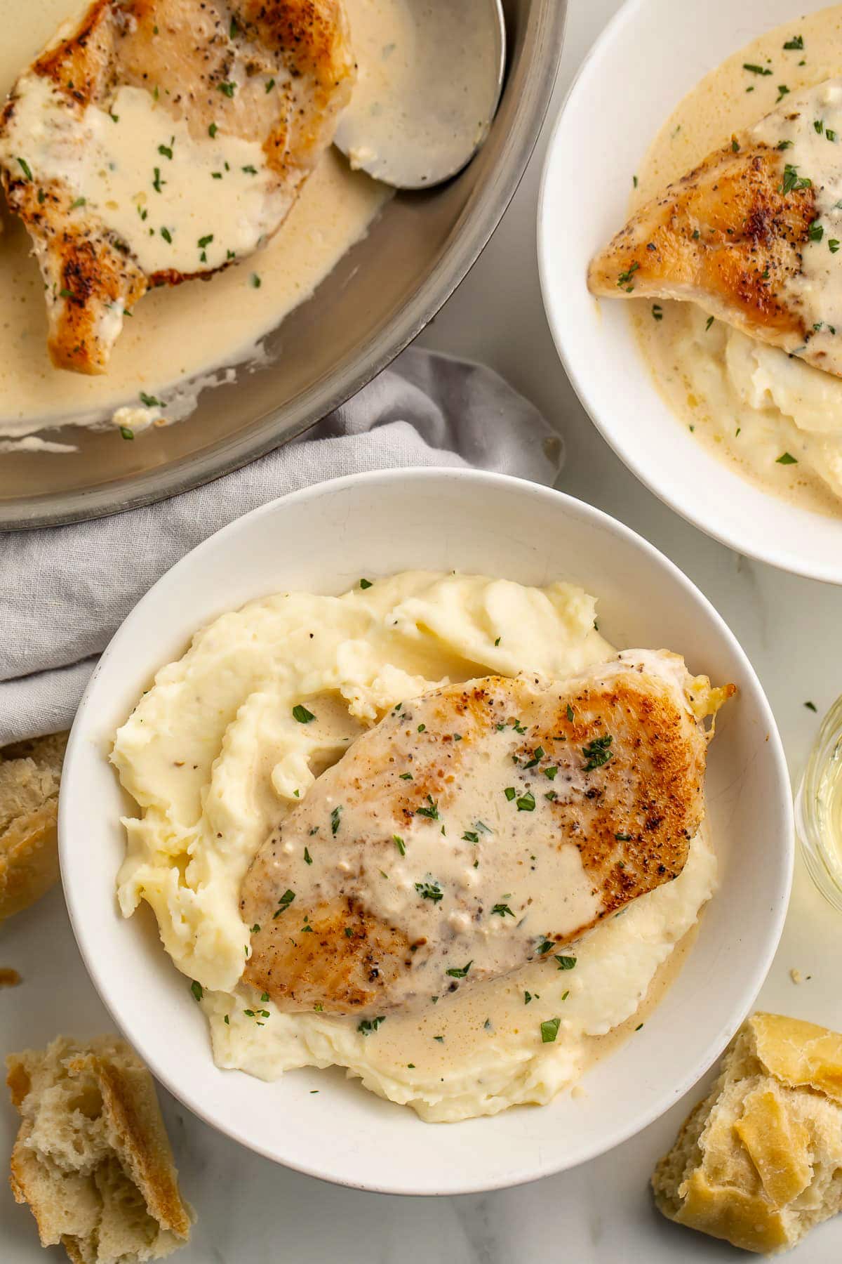 Top-down look at two bowls of mashed potatoes topped with cream cheese garlic skillet chicken and creamy sauce next to a large skillet.