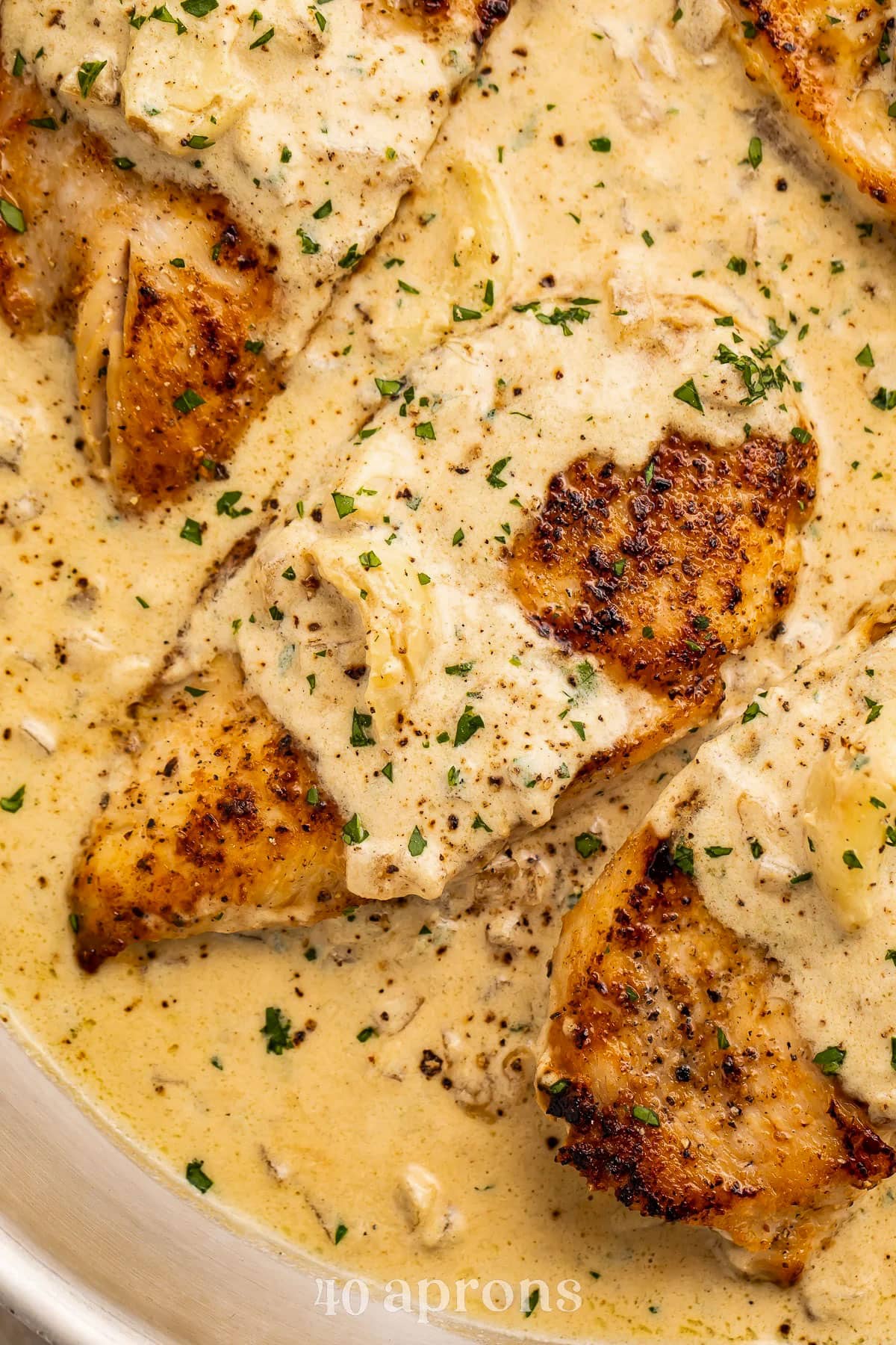 Close-up of a chicken breast swaddled in a creamy garlic sauce, resting in a large silver skillet.