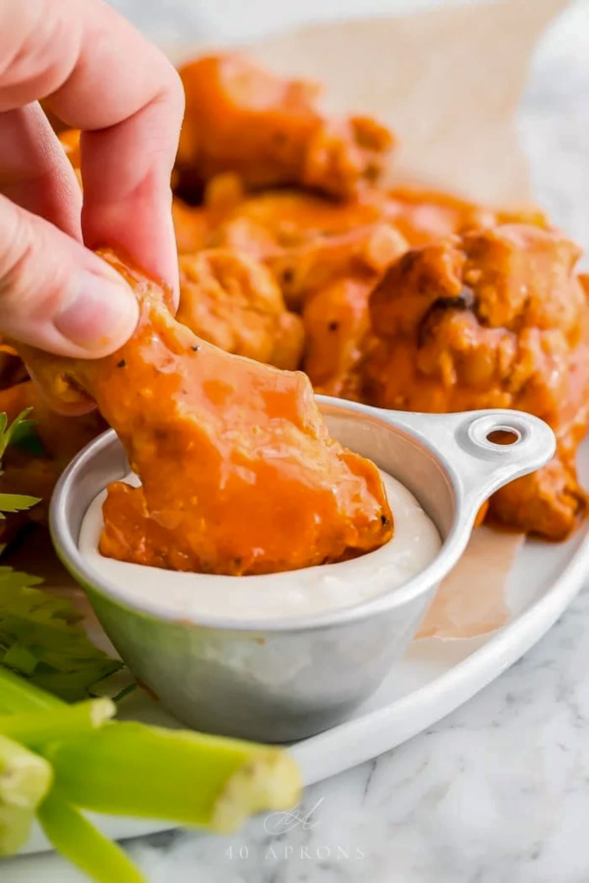Bright orange buffalo-sauced chicken wings, cooked in the Crockpot, being dipped into a small bowl of ranch dressing.