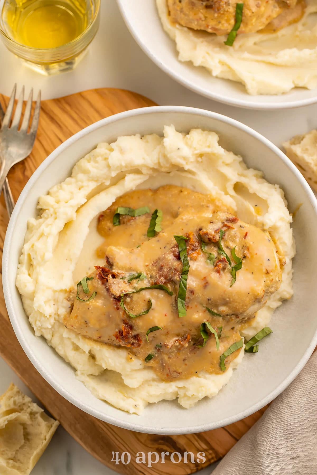Crockpot marry me chicken topped with basil and sun-dried tomatoes on a bed of mashed potatoes.