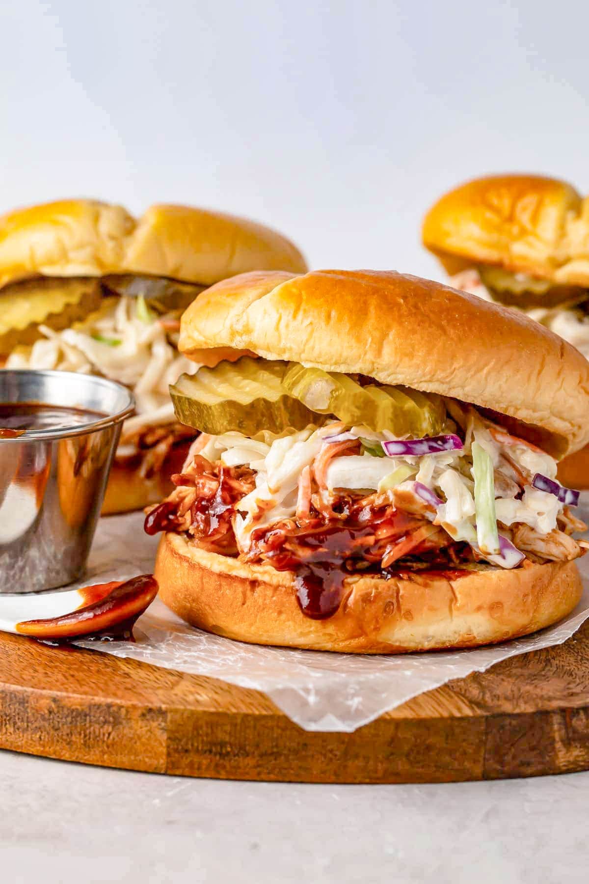 Instant Pot pulled bbq chicken sandwiched between two hamburger bun halves with coleslaw and pickles.