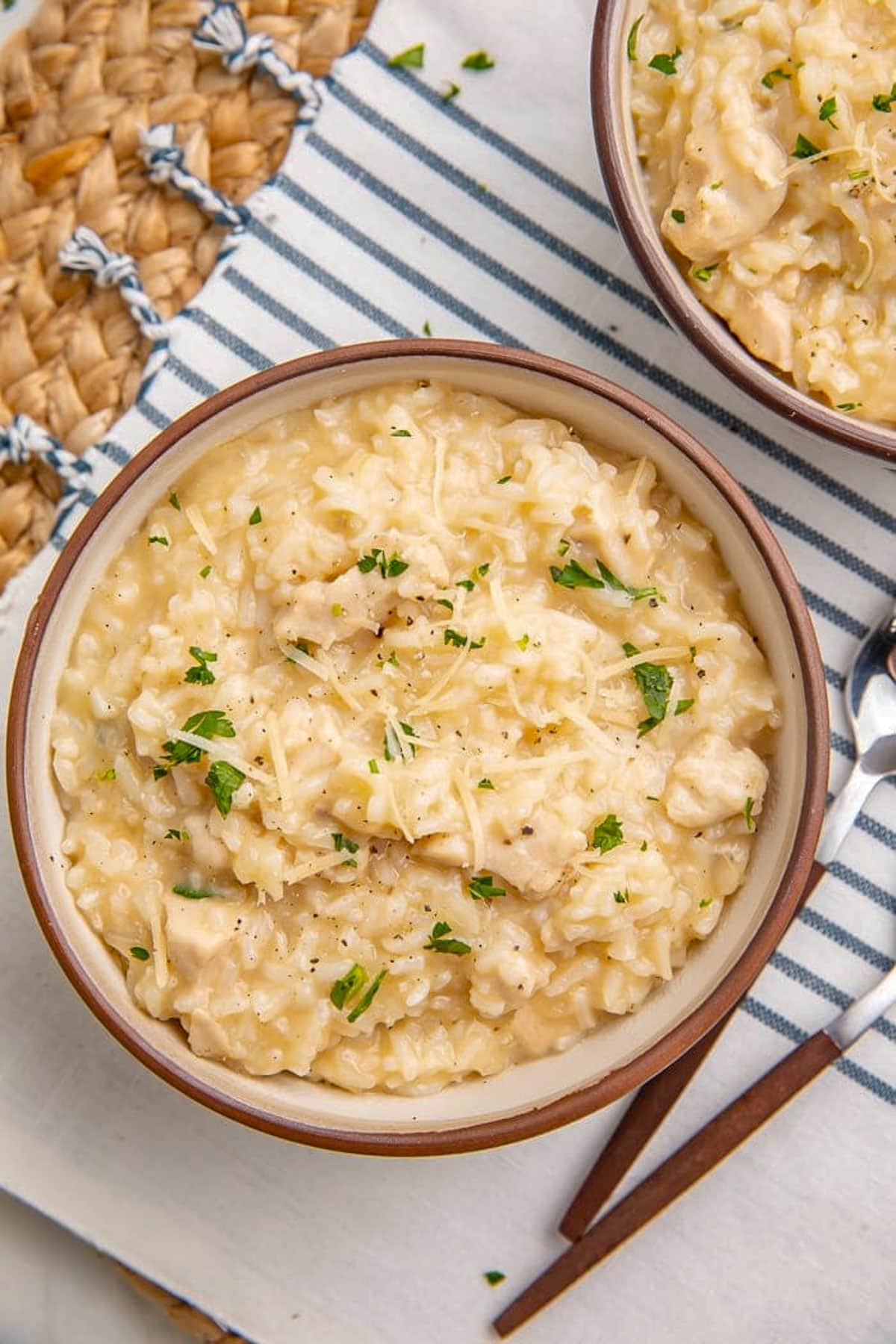 Two bowls of creamy chicken and rice cooked in an instant Pot on a table with a blue and white striped cloth napkin.