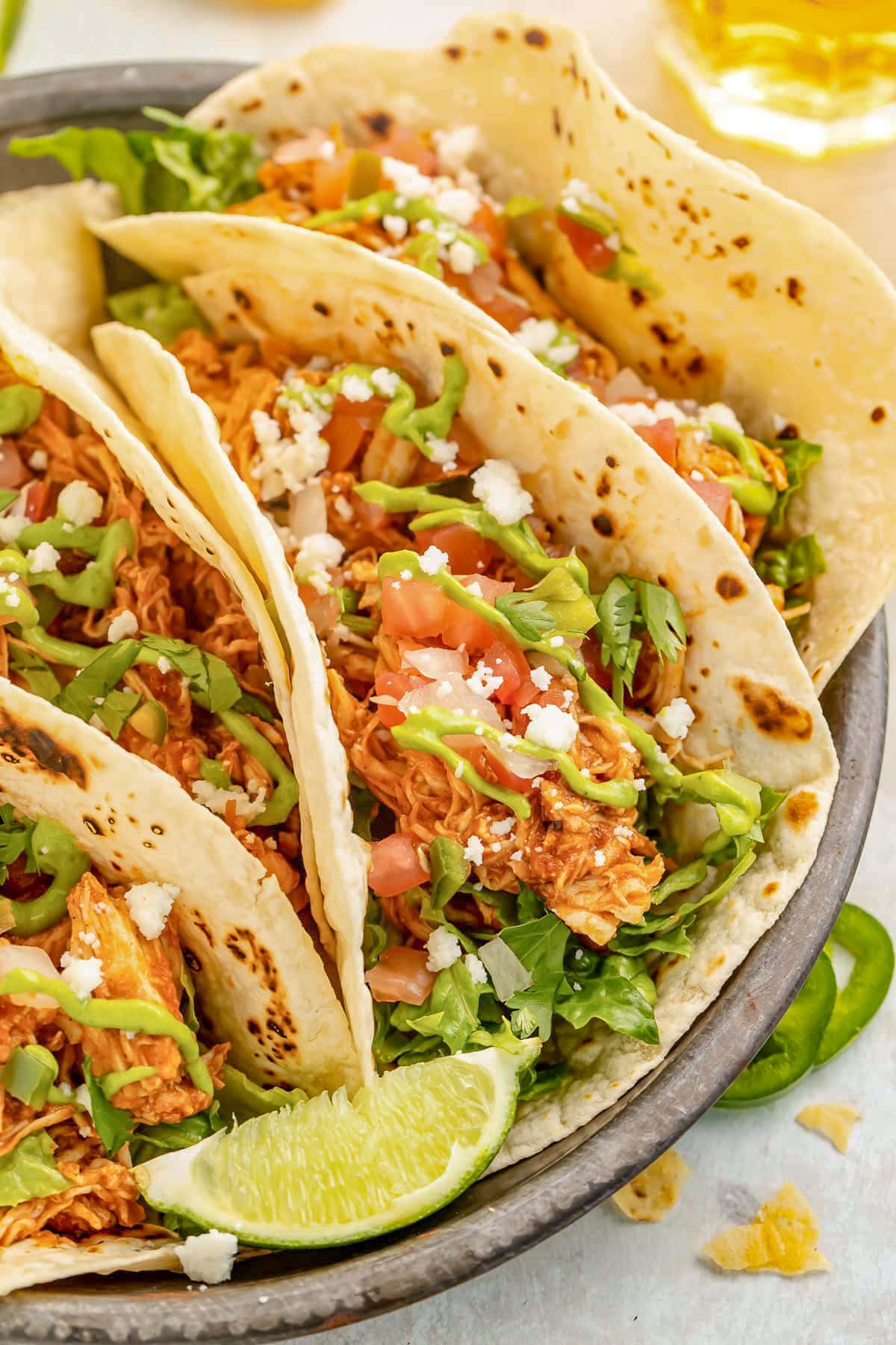Close-up of Instant Pot chicken tacos with flour tortillas, lettuce, crumbled queso, pico, and a lime wedge.