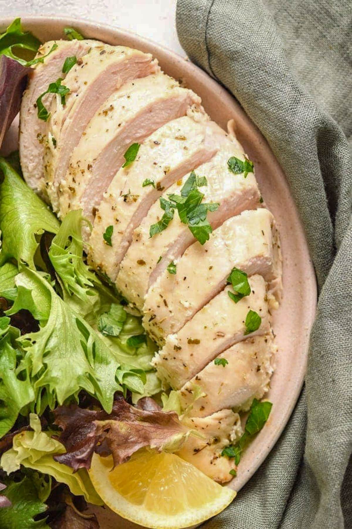An Italian dressing chicken breast, sliced into thick pieces, plated with a small green leaf salad.