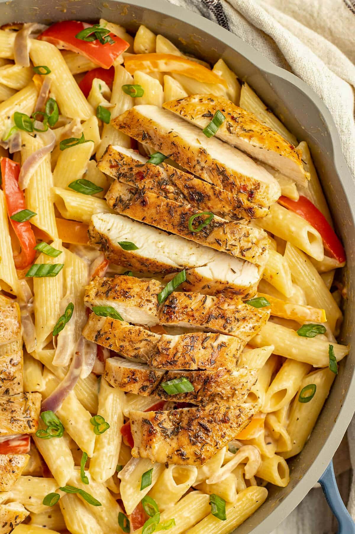 Jerk chicken pasta in a large skillet with fresh herbs, red tomato, and creamy penne.