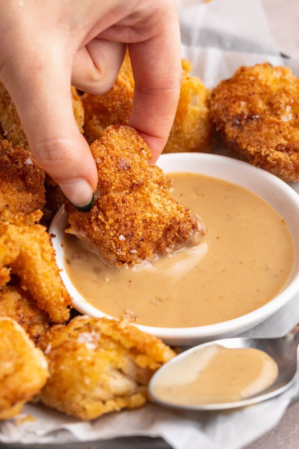 A white woman's hand dipping a breaded keto chicken chunk into a bowl of keto honey mustard sauce.