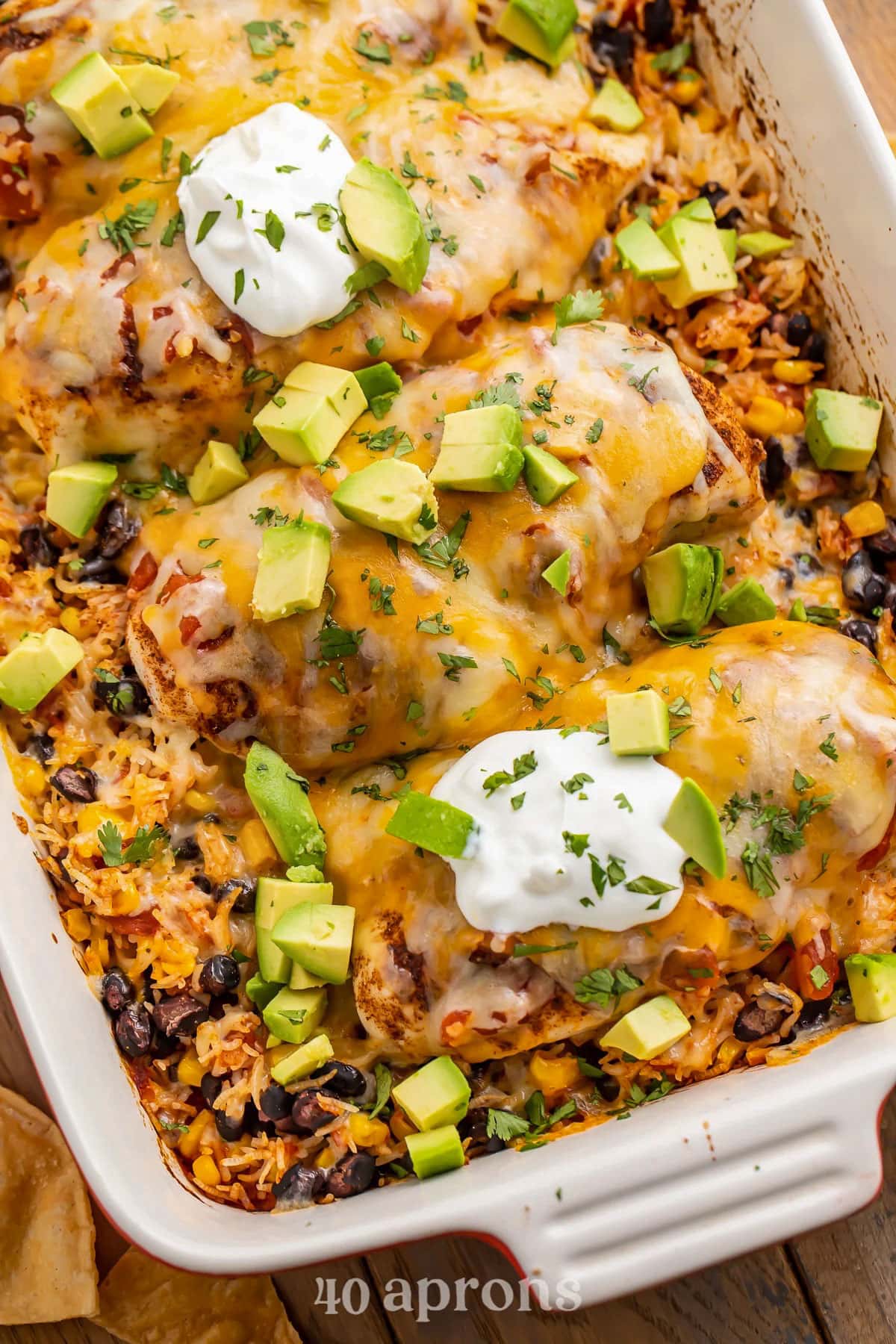 A casserole dish holding Mexican chicken casserole with rice, beans, and veggies, topped with avocado and sour cream.