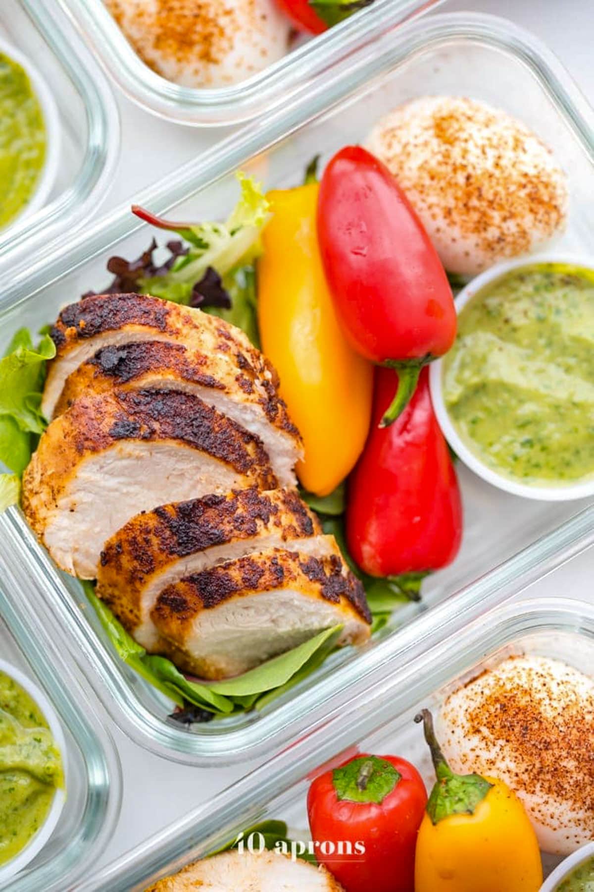 A glass meal prep container with sliced grilled chicken, bright red and yellow peppers, guacamole, and a bed of lettuce.