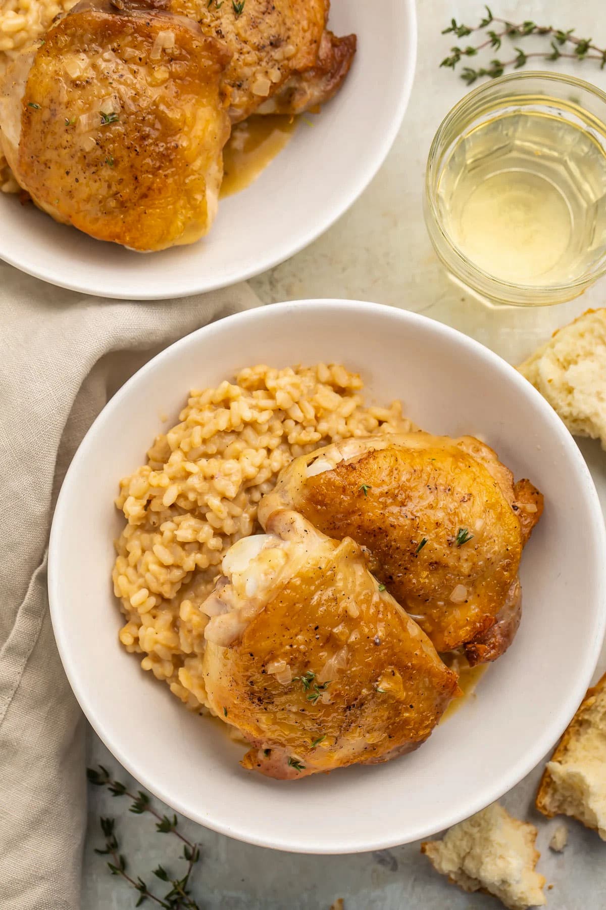Top-down photo of pan-seared chicken thighs in large white shallow bowls with creamy risotto.