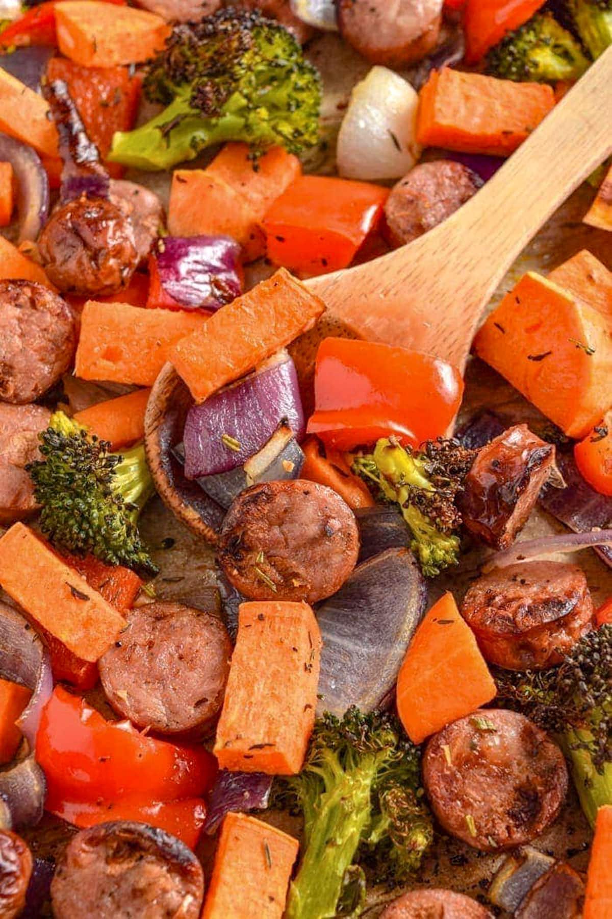 Easy sheet pan chicken sausage and roasted vegetables on a sheet pan with a large wooden spoon.
