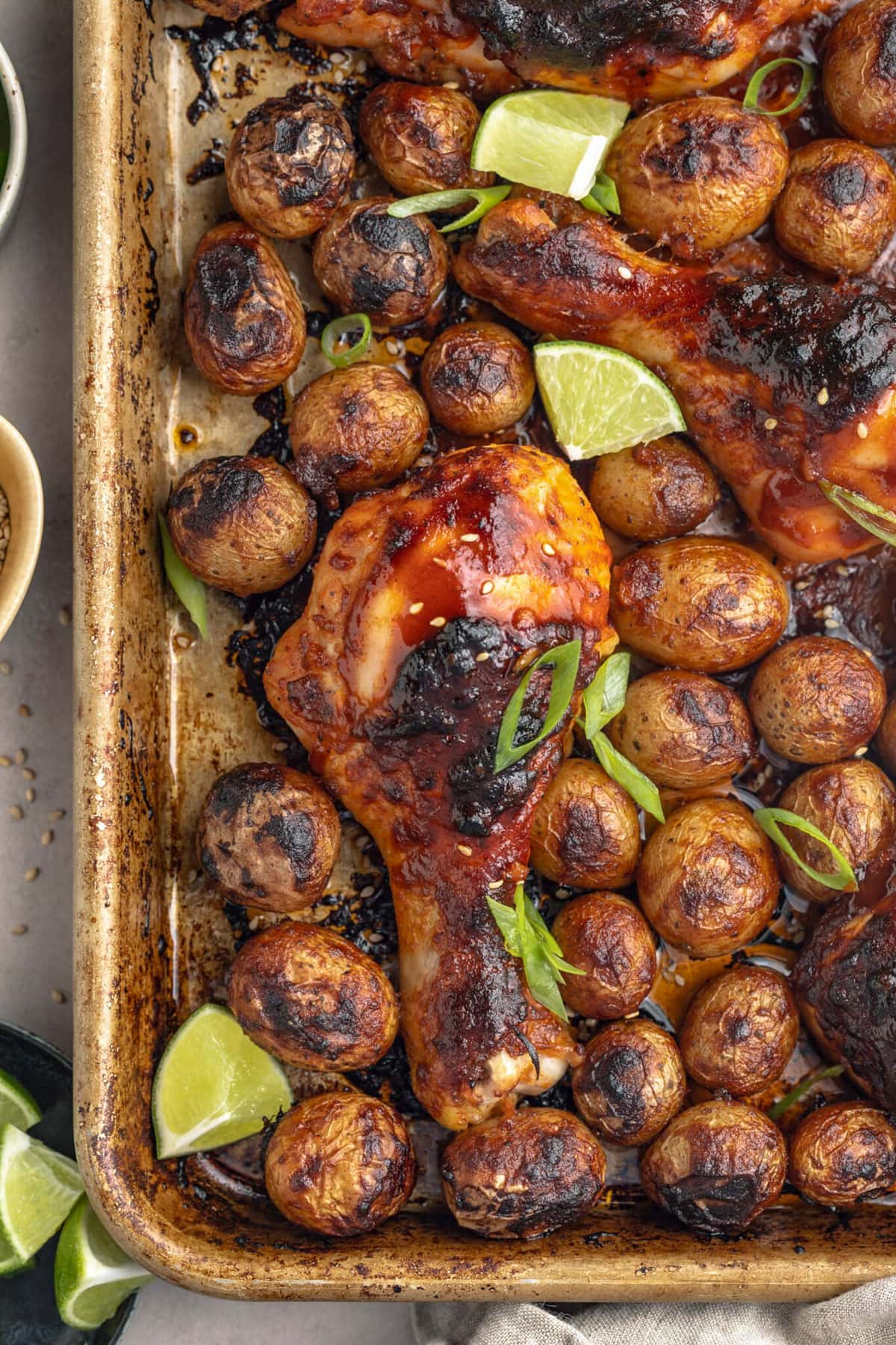 A baking sheet holding sheet pan gochujang chicken with potatoes and lime wedges.