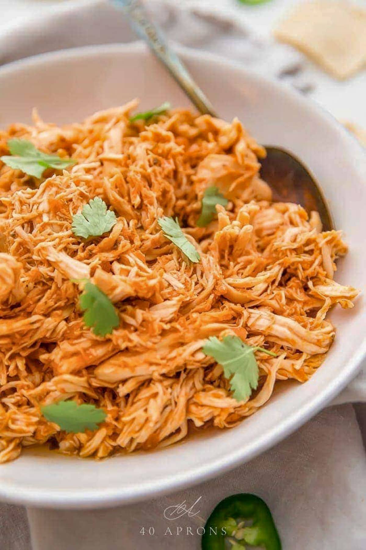 3 ingredient slow cooker Mexican shredded chicken garnished with green parsley in a white bowl.