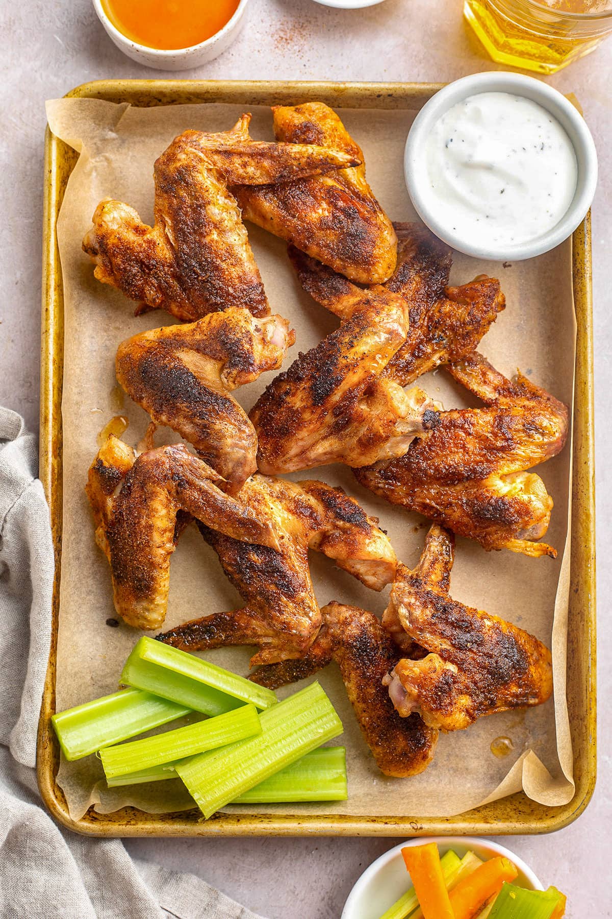 Seasoned, baked crispy whole chicken wings on a sheet pan with celery sticks and a ramekin of ranch dressing.