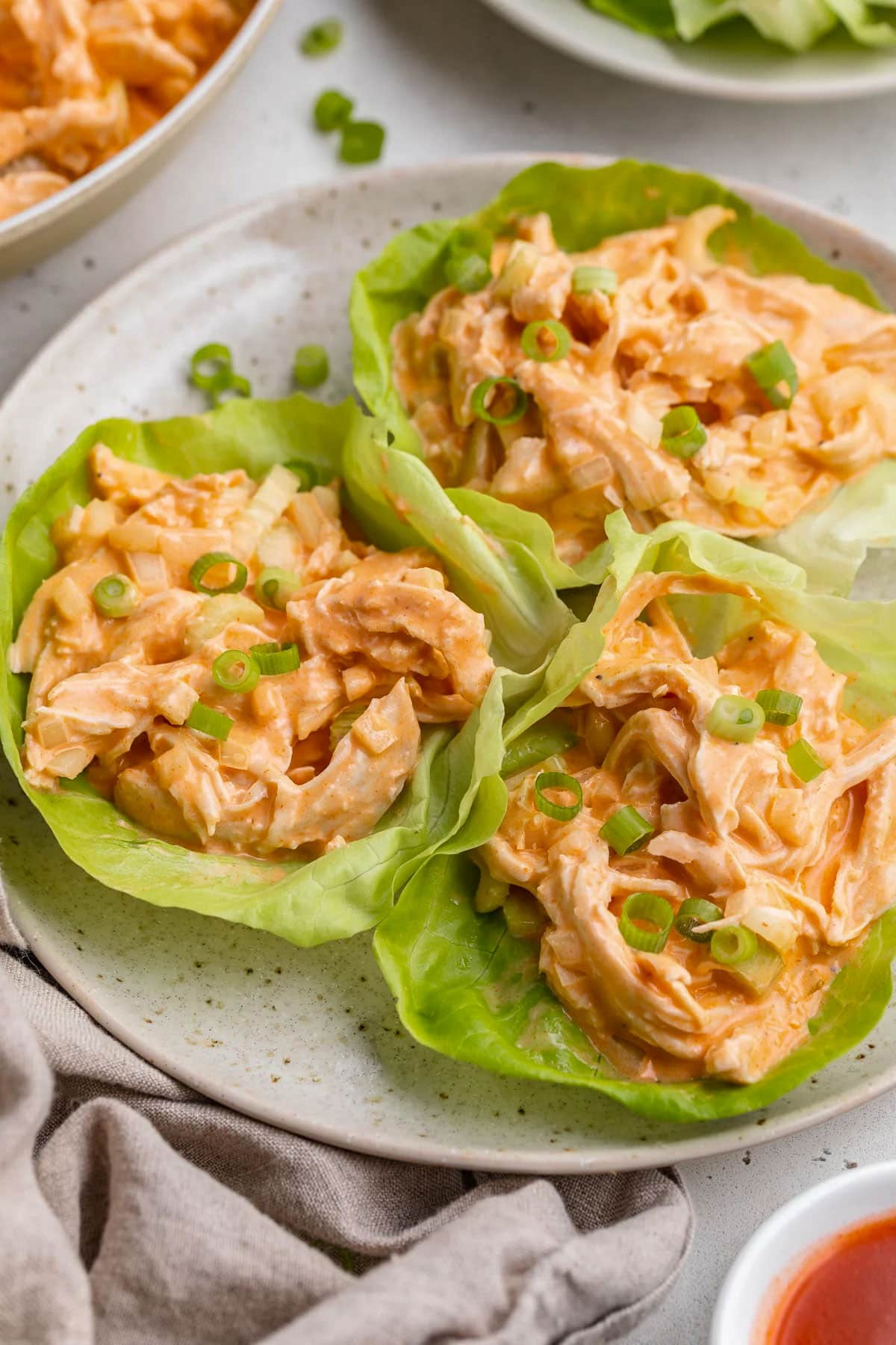 Whole30 buffalo chicken salad scooped into 3 lettuce cups and plated on a round plate.