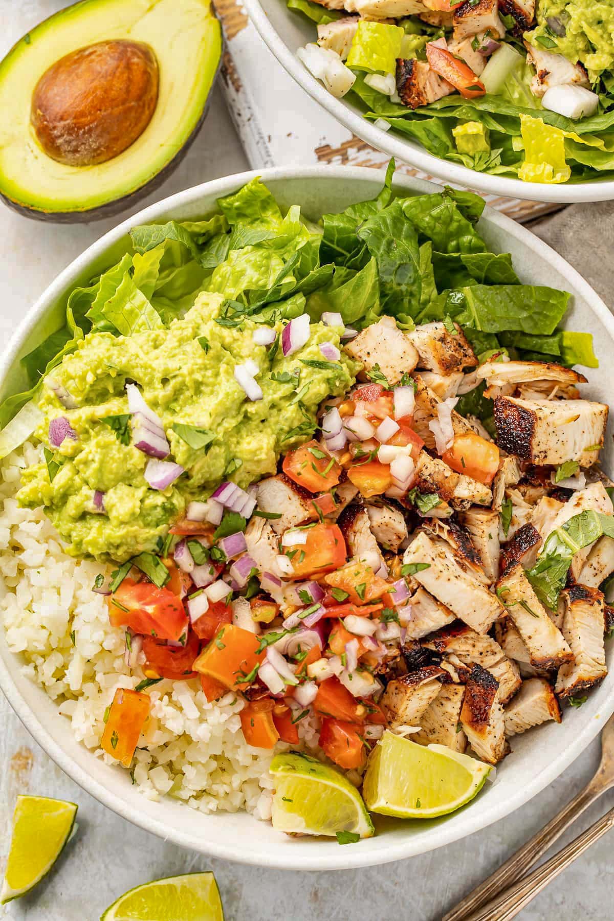 Close-up of a loaded burrito bowl with cauliflower rice, easy guacamole, fresh pico, grilled chicken, and green lettuce.