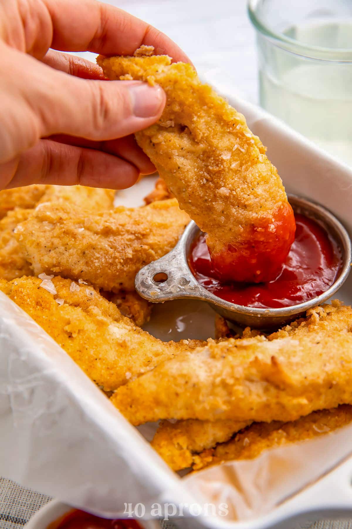 A Whole30 chicken tender being dipped into a ramekin of ketchup in a tray surrounded by other chicken tenders.