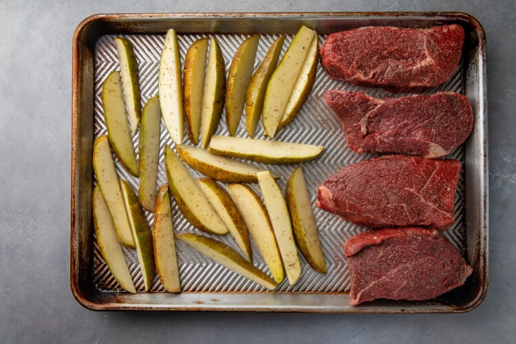 Uncooked steak and fries on baking sheet