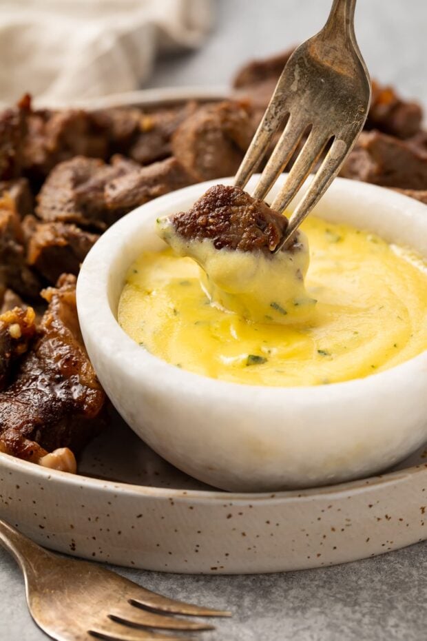 Garlic steak bite on the end of a fork, being dipped into a small bowl of microwave bearnaise sauce